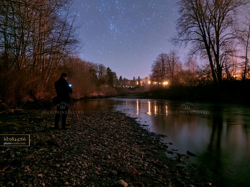 Photographer capturing stars beside a riverbank at night