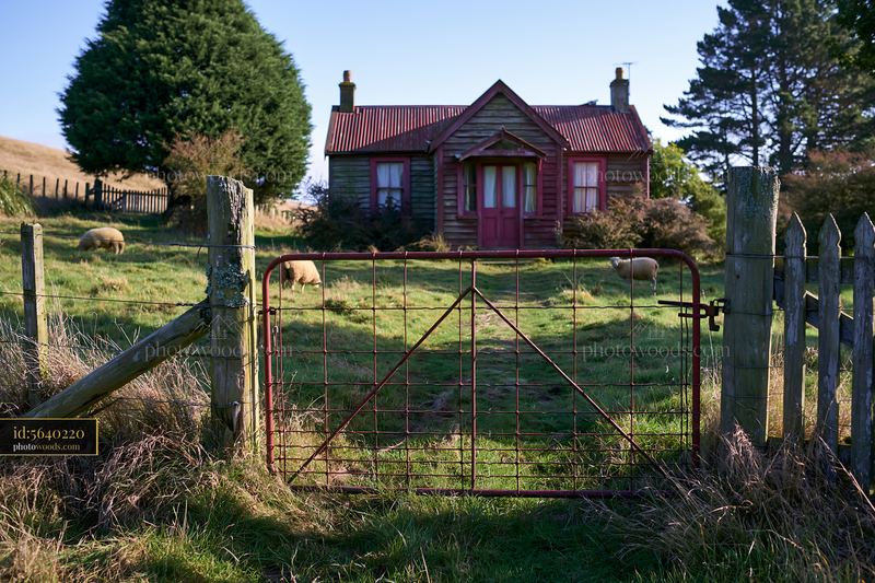 Rural cottage viewed through gate in grassy landscape