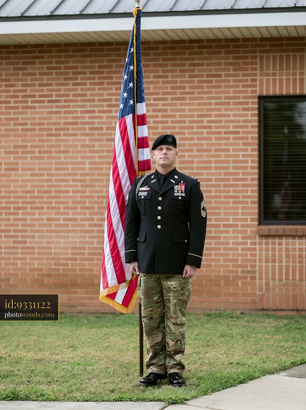 Sergeant standing at attention with American flag beside a building