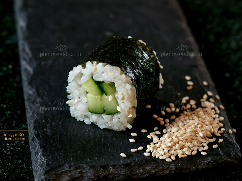Single sushi piece on black slate with sesame seeds