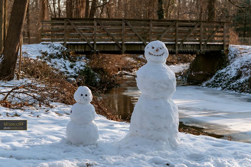 Small snowman beside a large snowman in a snowy park setting