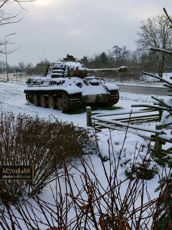 Soldier under camouflage netting by a snow-covered tank