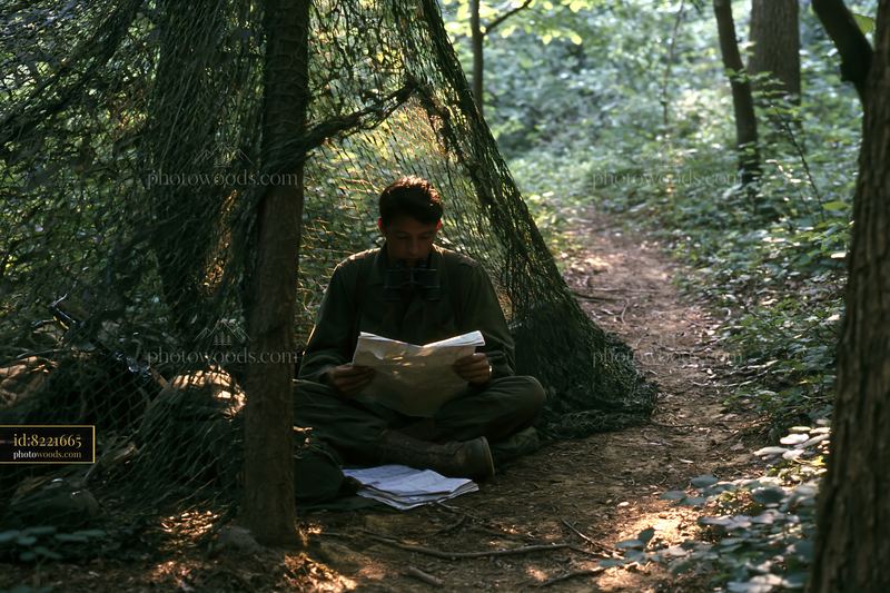 Soldier under camouflage netting reading in a forest setting
