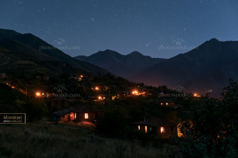 Starry night above a tranquil mountain valley with glowing houses