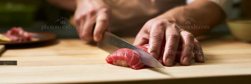 Hands of sushi chef cutting nigiri close up on wooden board