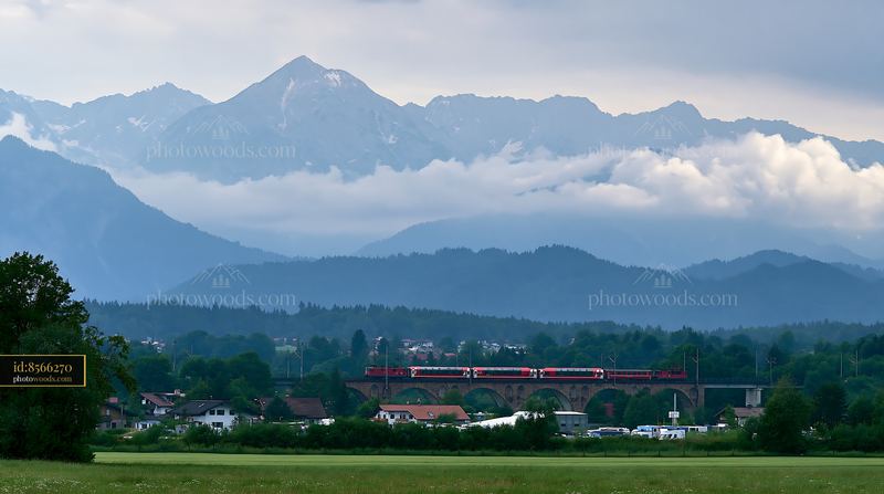 Dramatic clouds around alpine peaks and train moving through landscape