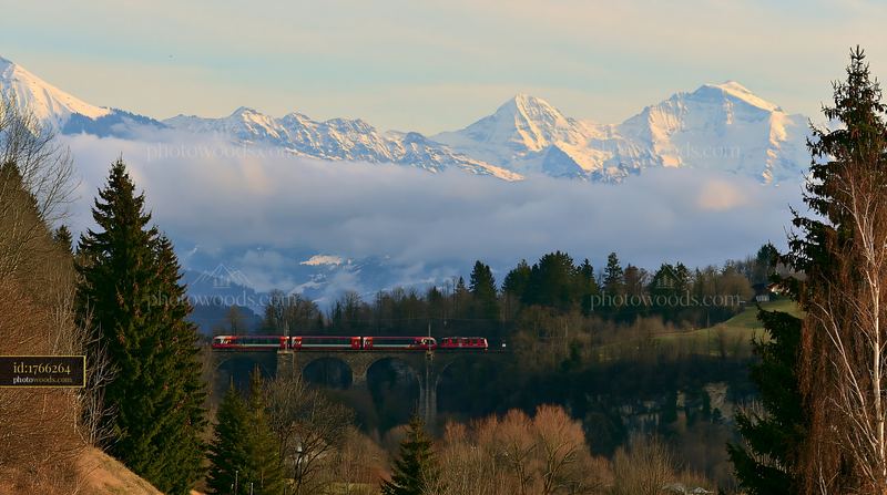 Train travels on a viaduct with dramatic clouds around alpine peaks