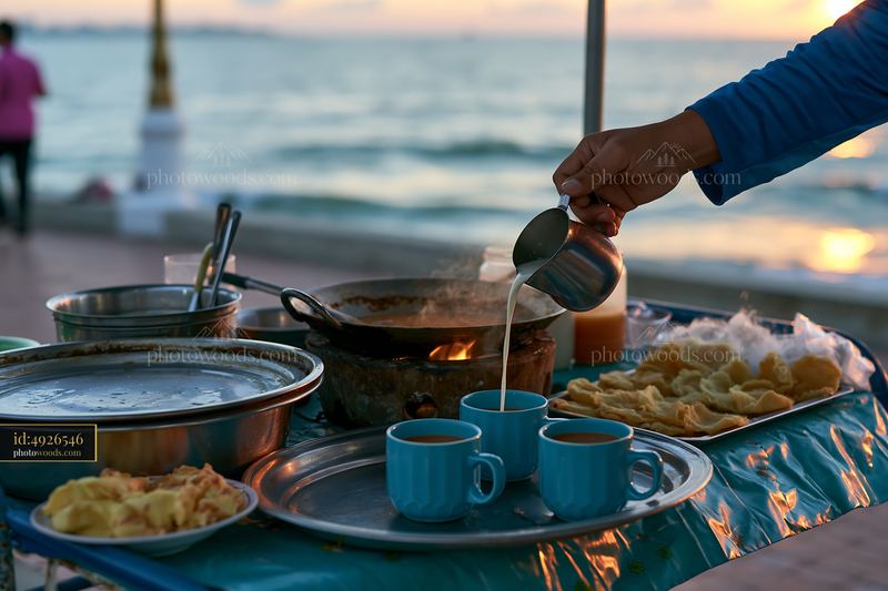Street food vendor adds milk to tea by the seaside at sunset