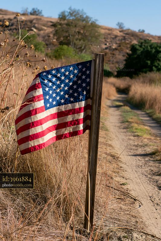 Weathered American flag along a dusty trail in grassy fields