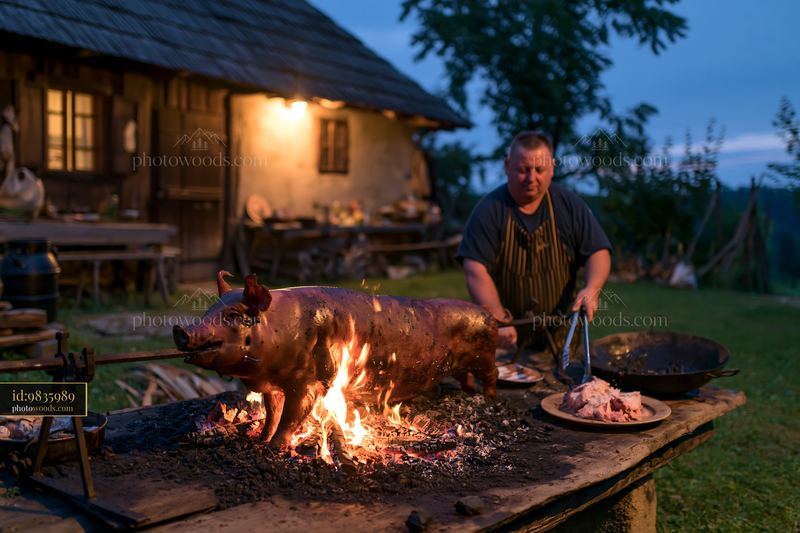 Whole suckling pig roasting over a charcoal grill at sunset