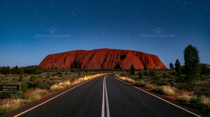 Uluru under a starry night sky with a winding road