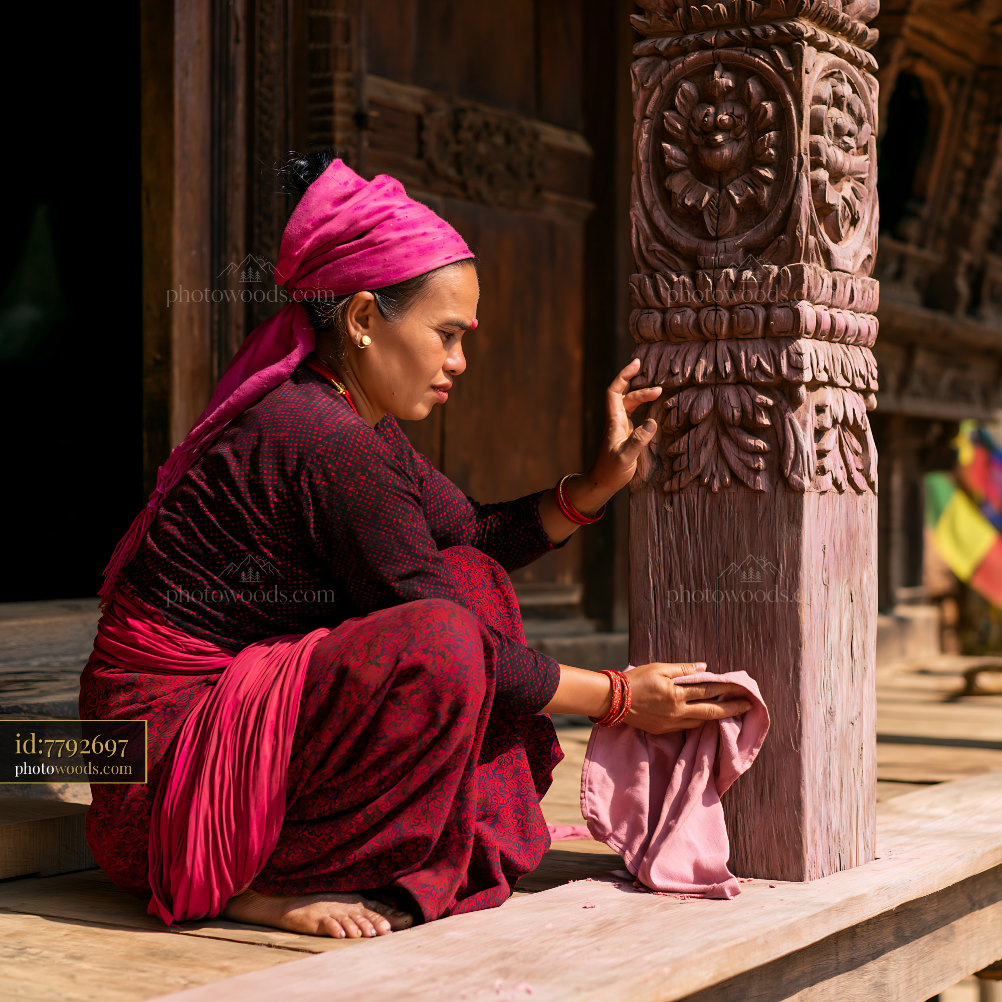 A woman in heritage attire is decorating a wooden house while sitting on the steps.