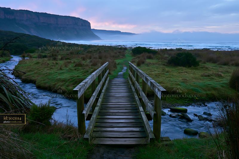 Coastline beneath dramatic cliffs at dusk with wooden bridge