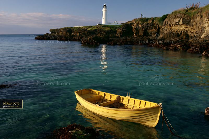 Lighthouse with boats in the foreground and rocky coastline