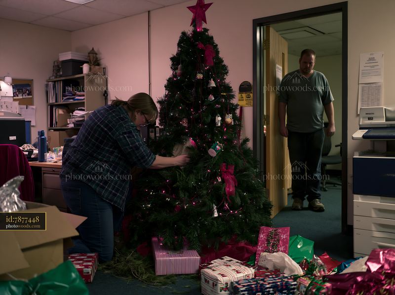 Adults decorating a Christmas tree with wrapped gifts in an office