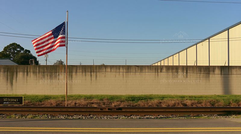 American flag waving outside factory alongside railroad tracks