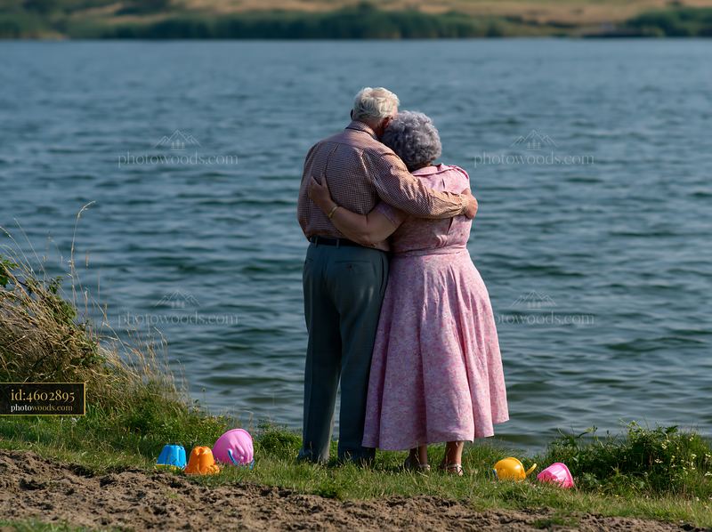 Elderly couple embracing beside a lake with colorful toys