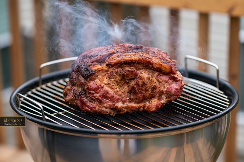 Roast pork cooking on a barbecue grill with smoke rising