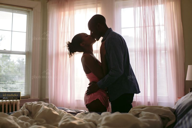 Couple kissing in a bright bedroom beside an unmade bed