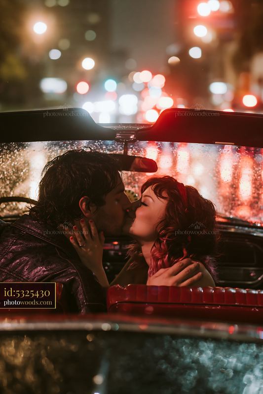 Couple kissing inside a vintage car on a rainy night