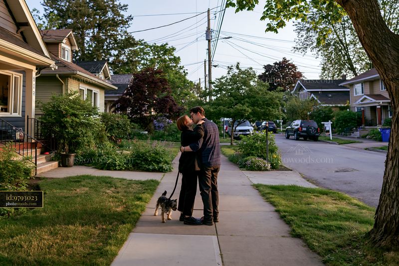 Couple kissing on a residential sidewalk with their dog