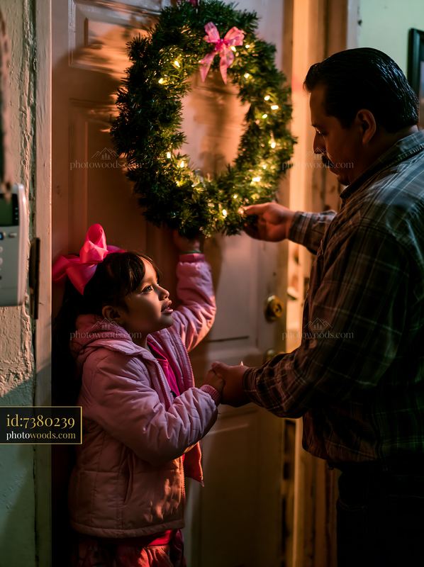 Father and daughter hanging a lit Christmas wreath on a door