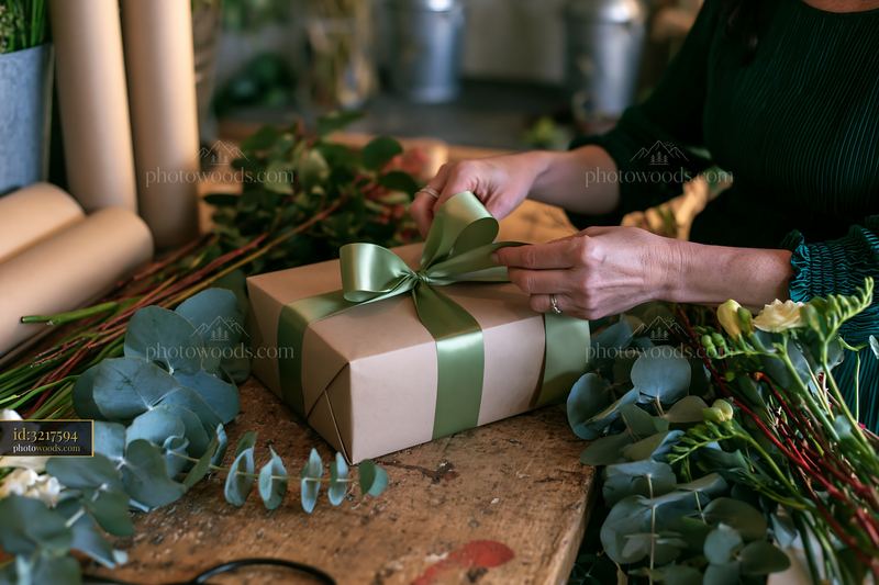 Hands tying a green ribbon around a wrapped gift box