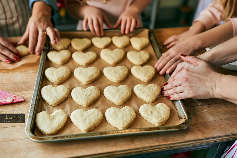 Heart-shaped cookies arranged on a baking tray with hands nearby