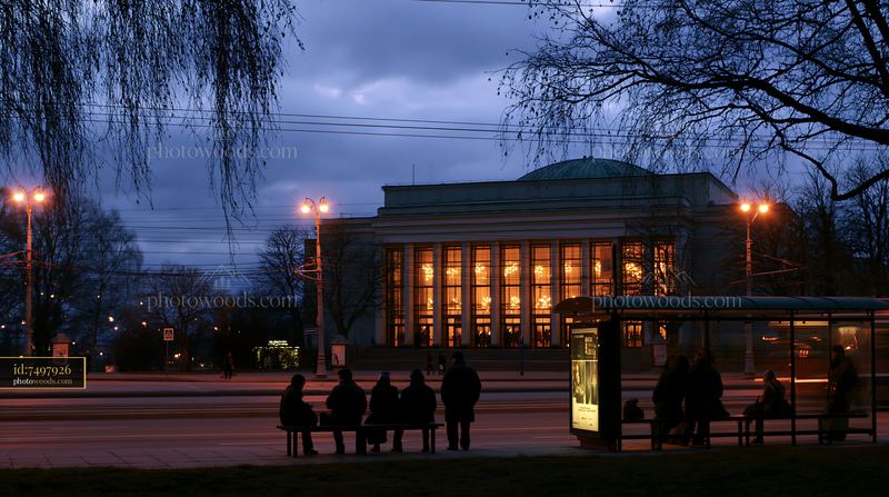 Illuminated theater exterior at dusk beside a city bus stop