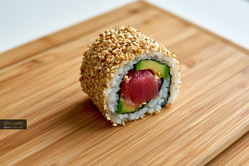 One tuna roll slice with sesame coating on a wooden board