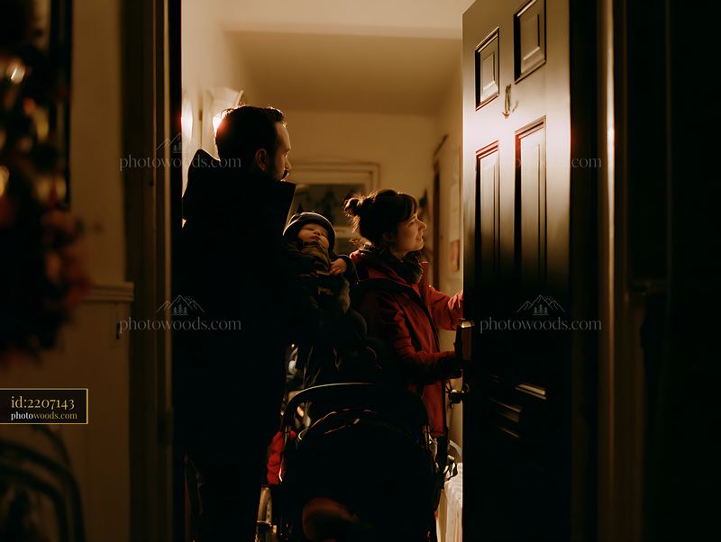 Parents carry a sleeping child through a warmly lit home