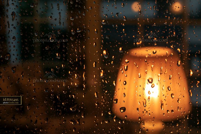 Raindrops on cottage window with warm lamp glow