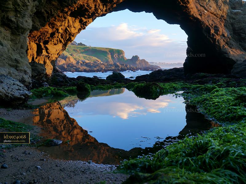 Rocky sea cave framing a coastal landscape and reflective tide pool