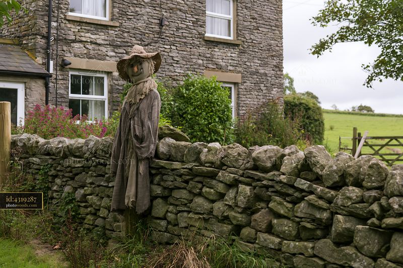 Rustic scarecrow beside a stone farmhouse and field