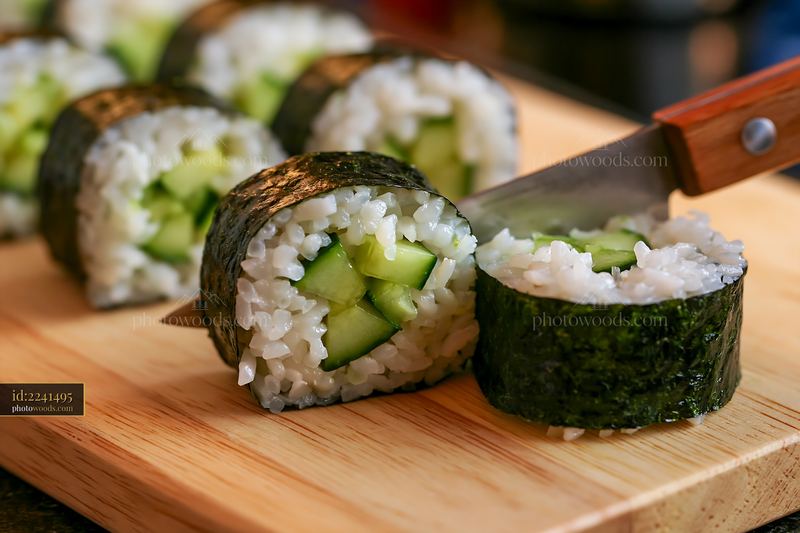 Sushi rolls being cut with knife on a wooden board