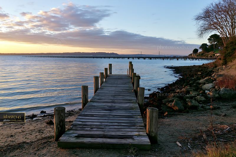 Coastline with mussel farms near a wooden pier at sunset