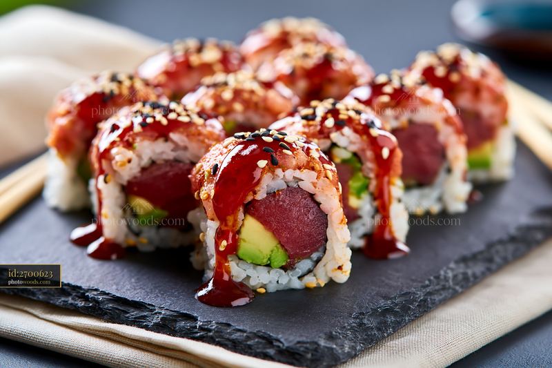 Spicy tuna roll close-up with sesame and sauce on a black slate