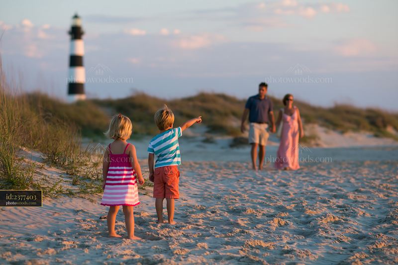 Family sightseeing on a sandy beach near a striped lighthouse