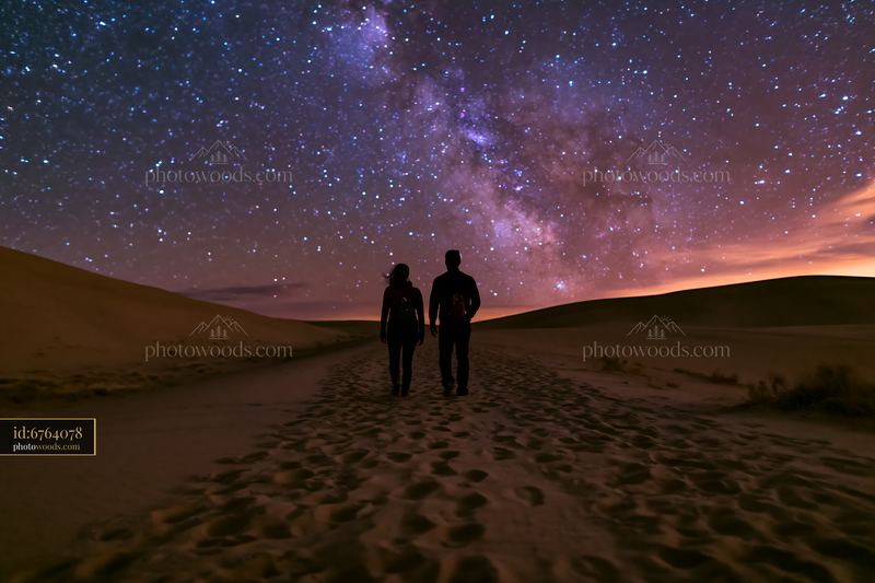 Couple Walking Across Sand Dunes Beneath a Starry Night Sky