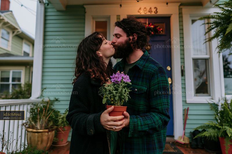Couple kissing while holding a flowering plant outside their home