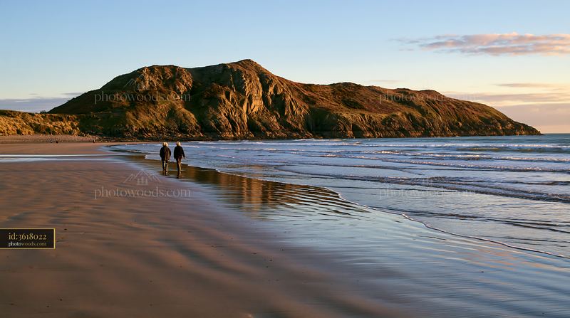 Coastline with rocky peninsula at sunset with two people walking