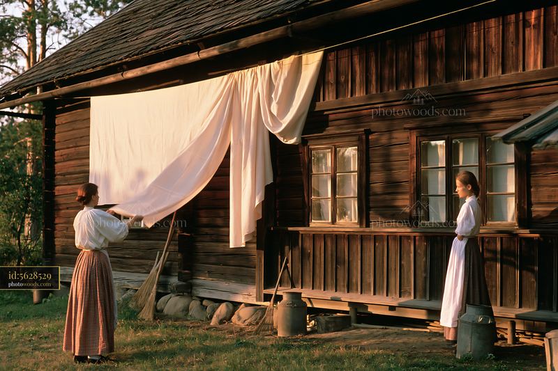 Two women decorating a rustic wooden house with fabric