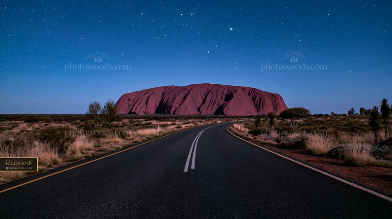 Uluru under a starry night sky with a clear road in view