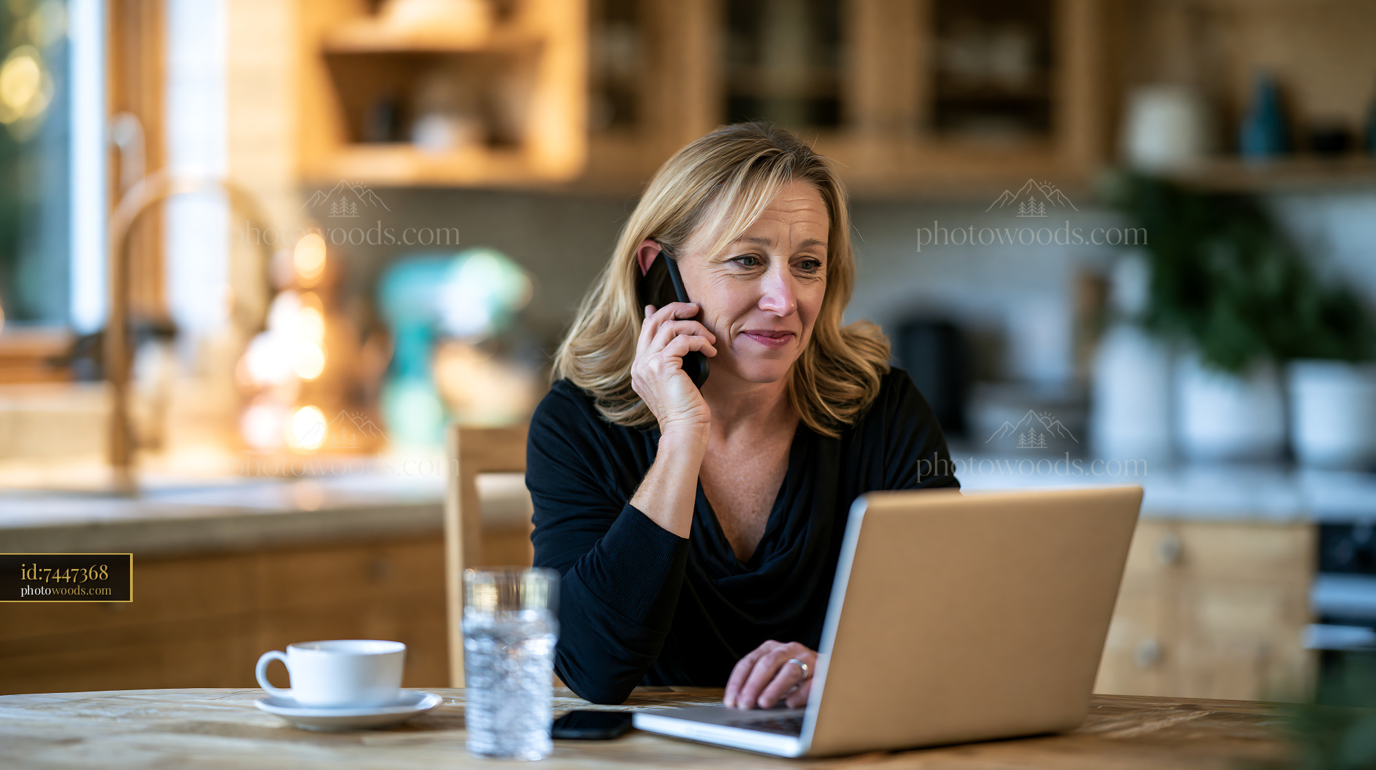 Woman Using Laptop While Talking on Phone in Kitchen Setting