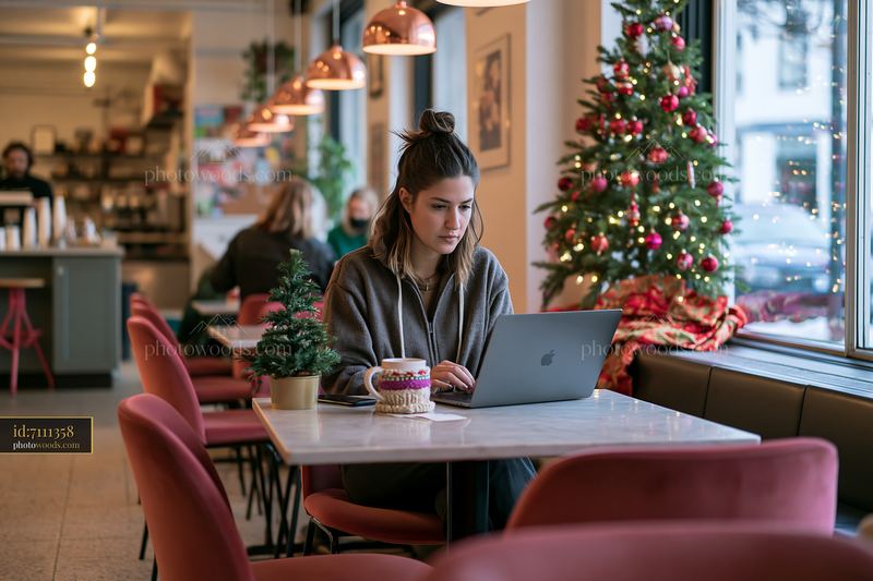 Woman working on laptop in festive coffee shop interior