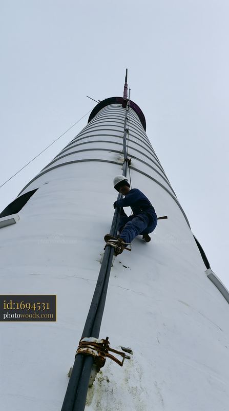 Worker climbing a lighthouse exterior for maintenance