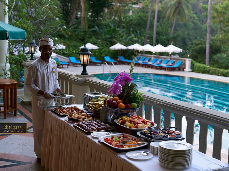 Buffet table set up near a swimming pool with food and staff