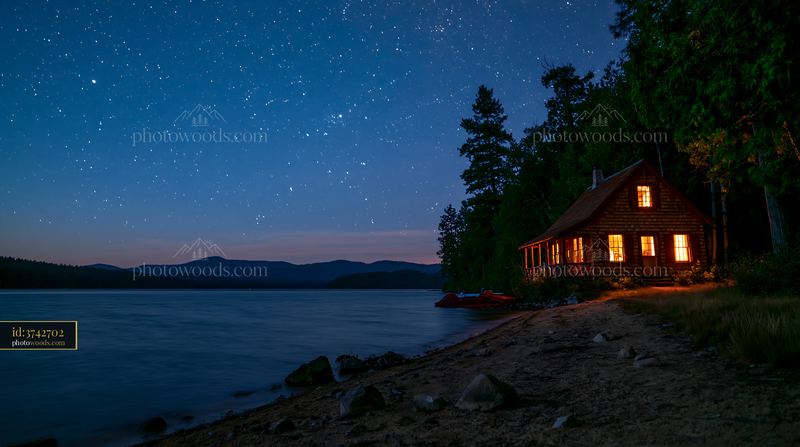 Cabin under stars viewed from a lake shore
