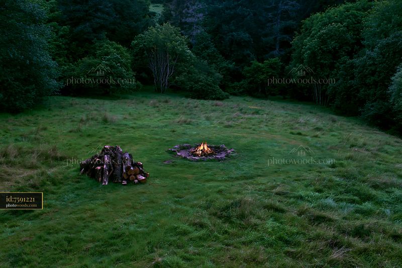 Meadow viewed from above with a campfire and log pile