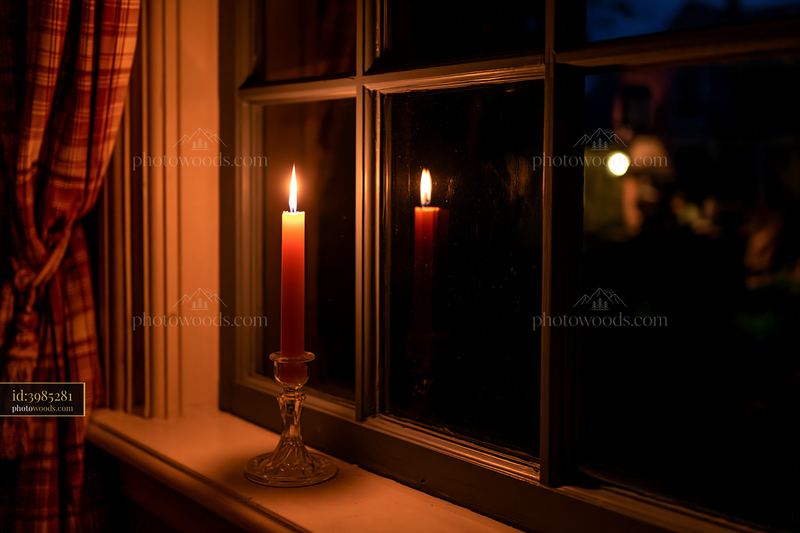 Candle with light on windowsill beside glass windowpane